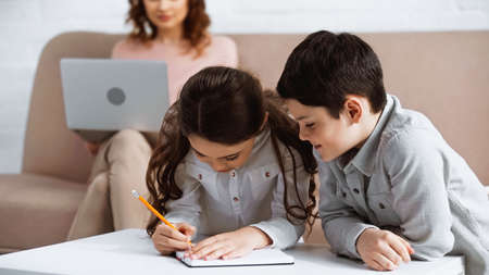 Kids doing homework on notebook near mother with laptop on blurred background