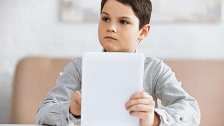 Preteen boy holding digital tablet on blurred foreground during online education
