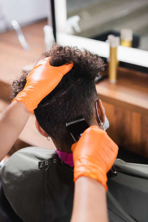 Hairdresser in latex gloves trimming back of head of african american clientの写真素材