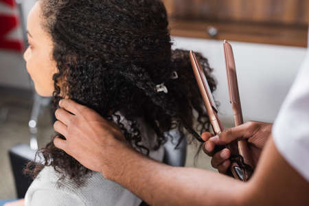 African american hairdresser holding hair straightener near clientの写真素材