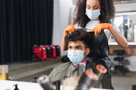 African american hairdresser in latex gloves and medical mask cutting hair of clientの写真素材