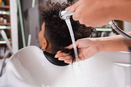 African american hairdresser washing hair of client near sinkの写真素材