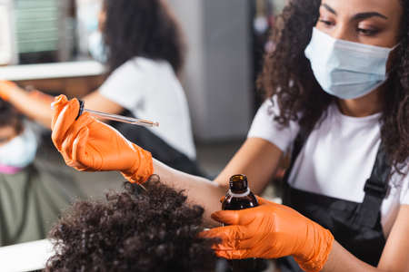 Cosmetic oil in hands of african american hairdresser in latex gloves and client on blurred foregroundの写真素材