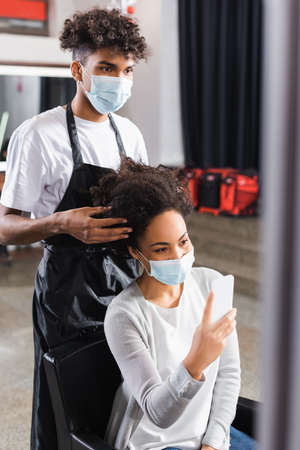 African american hairdresser touching hair of client with smartphoneの写真素材