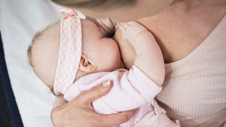 mother feeding with breast baby girl in headband with bow