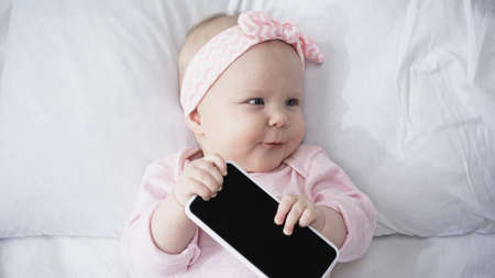 top view of infant baby holding smartphone with blank screen and looking away