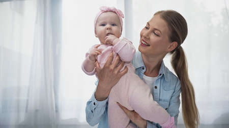 positive woman holding in arms infant daughter in headband with bow