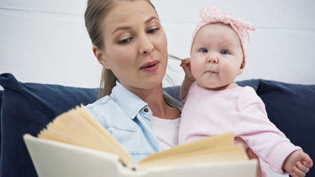 attractive mother reading book to infant baby girl daughter