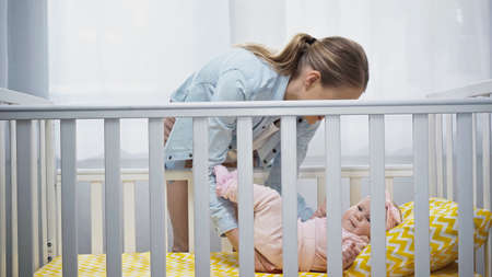 happy mother putting infant baby in baby crib