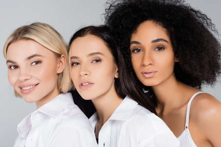 young interracial women with perfect skin looking at camera isolated on gray