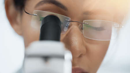 close up of african american scientist in glasses looking through microscope in lab