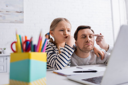 father helping thoughtful daughter doing homework near laptop on blurred foregroundの写真素材