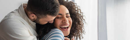 happy multiethnic couple hugging at home, banner