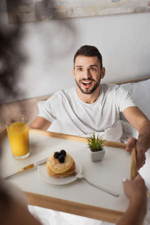 amazed man taking tray with breakfast from hands of african american girlfriend