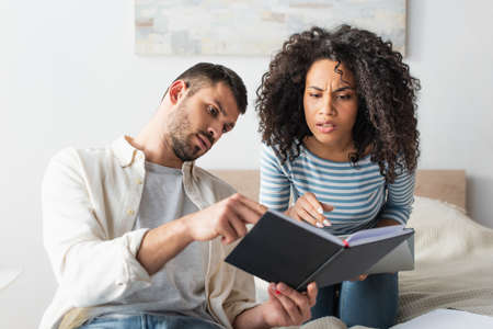 interracial couple looking at notebook in bedroom