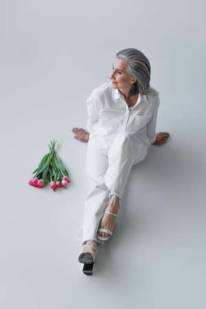 High angle view of woman in white clothes sitting near flowers on gray backgroundの写真素材