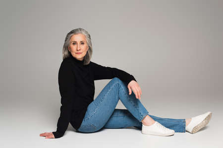 Middle aged woman looking at camera while sitting on gray background