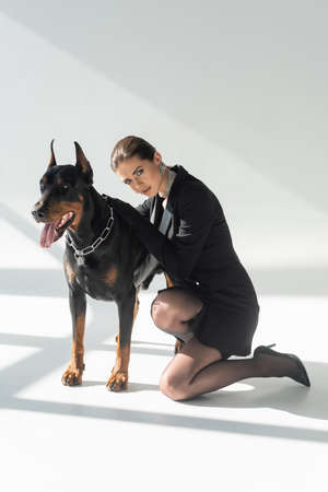 sensual, brunette woman leaning on doberman dog on gray background with shadowsの写真素材