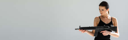 brunette woman in bodysuit aiming with rifle isolated on gray, banner