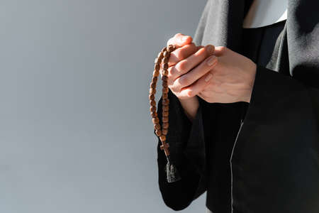 partial view of nun with prayer beads isolated on gray