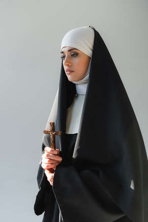 young nun in cassock holding crucifix isolated on grayの写真素材