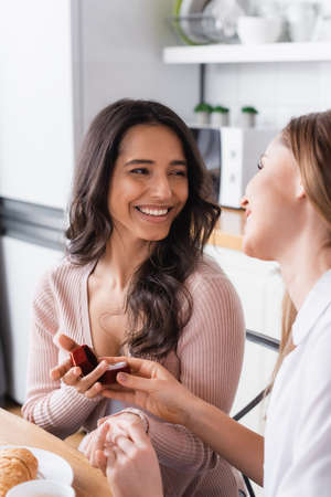happy girlfriends looking at each other and holding wedding ring, marriage proposal conceptの写真素材