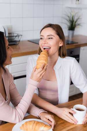 woman feeding happy girlfriend with tasty croissantの写真素材