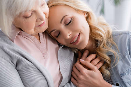 Senior woman hugging happy daughter at homeの写真素材