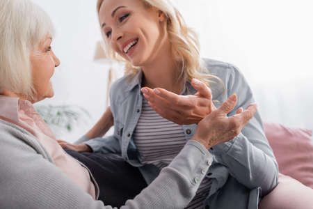 Senior woman sitting near smiling daughter talking on blurred backgroundの写真素材