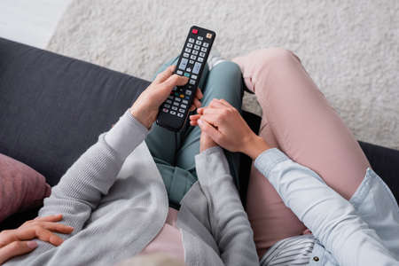 Top view of woman holding hand of senior mother with remote controller on couchの写真素材