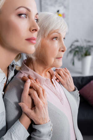 Elderly parent holding hands of daughter on blurred foreground at home