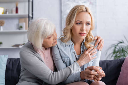 Senior parent embracing upset daughter with napkin on couchの写真素材