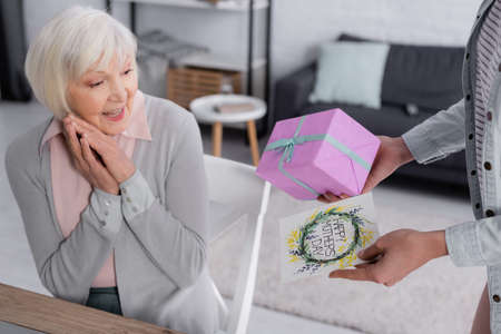 Woman holding greeting card and present near smiling mother
