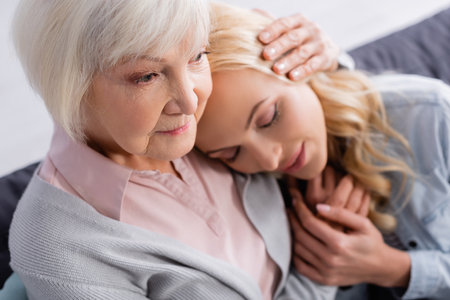 Elderly parent hugging adult daughter on blurred backgroundの写真素材