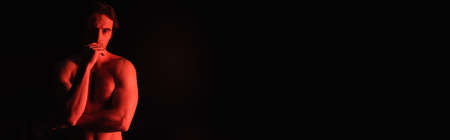 red lighting on sexy muscular man standing isolated on black, banner