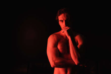 red lighting on sexy man standing isolated on blackの写真素材