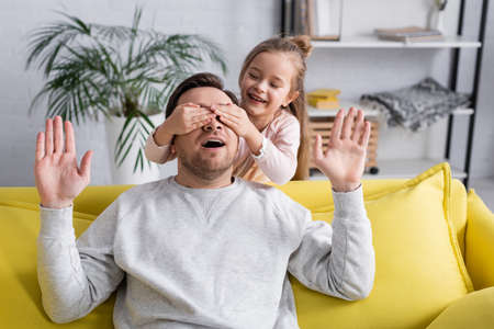 Smiling kid covering eyes of father at homeの写真素材