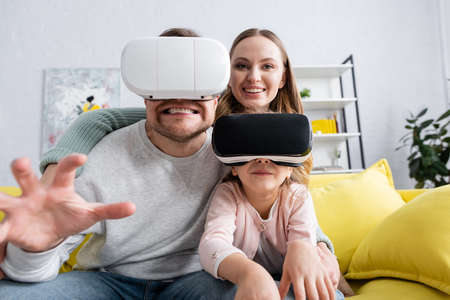 Kid and father gaming in vr headsets near smiling mom at homeの写真素材