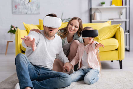 Excited man and daughter using vr headsets near mother at home