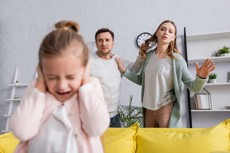 Man holding hair of wife during quarrel near scared daughter on blurred foregroundの写真素材
