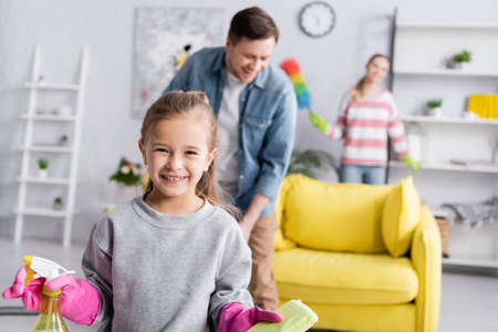 Girl with rag and detergent standing near parents on blurred backgroundの写真素材