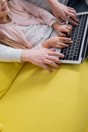 Cropped view of smiling kid using laptop near parents on yellow couchの写真素材