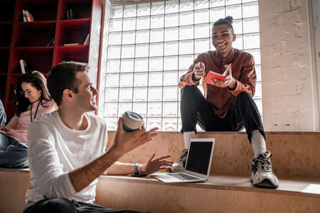 happy interracial students looking at each other near cheerful classmate