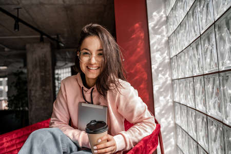 happy young student in glasses holding paper cup with coffee to go and e-book