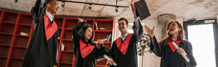 amazed interracial students in graduation gowns holding diploma, senior 2021, banner