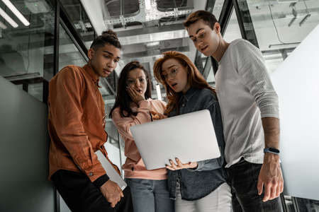 low angle view of shocked interracial students looking at laptopの写真素材