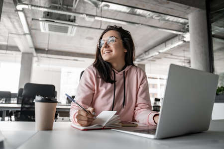 happy brunette woman in glasses looking away while holding pen