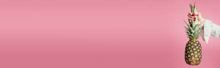 Cropped view of woman holding leaves of pineapple isolated on pink, bannerの写真素材