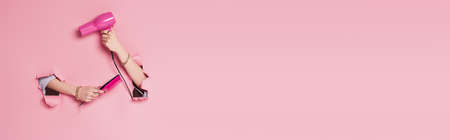 Cropped view of hair dryer and comb in hands woman near pink background with holes, bannerの写真素材