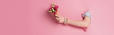 Cropped view of woman holding delicious waffle cone and rose flowers in hole of pink background, bannerの写真素材